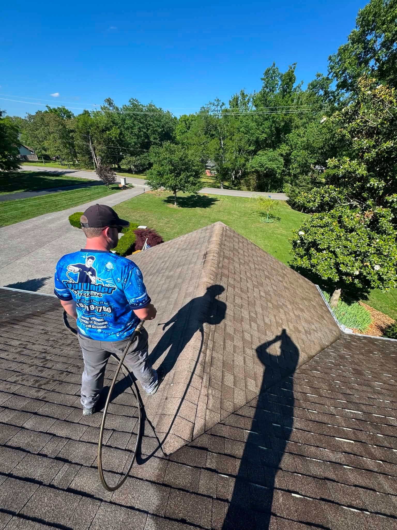 Cool Under Pressure technician soft washing a residential roof — treating algae and dark streaks on shingles